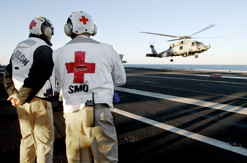 Two military medical professionals watch a helicopter land.
