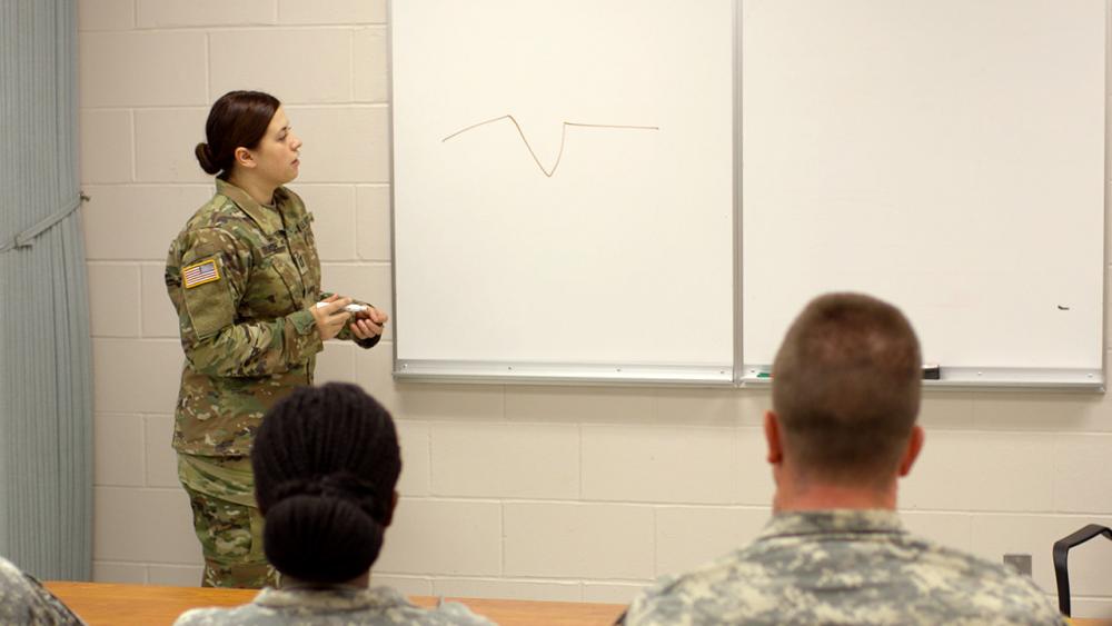 Sara standing at whiteboard giving a lesson to the class