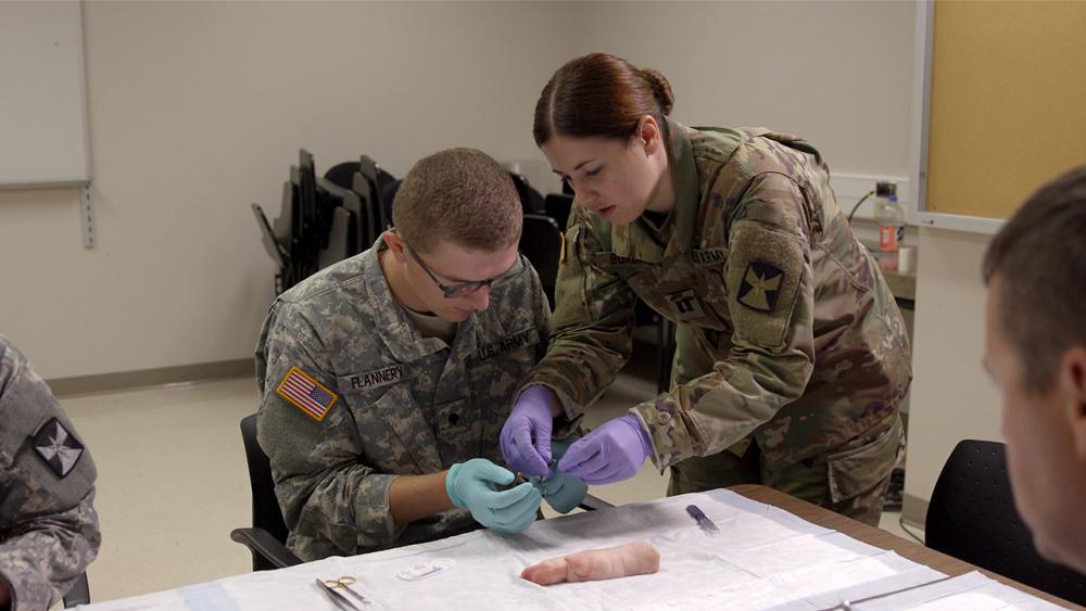 Sara showing a medic how to make a suture using a pig's foot