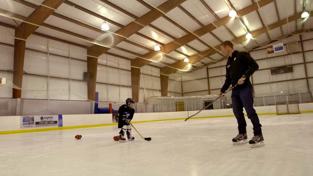 Hunter passes his son the puck on ice rink 